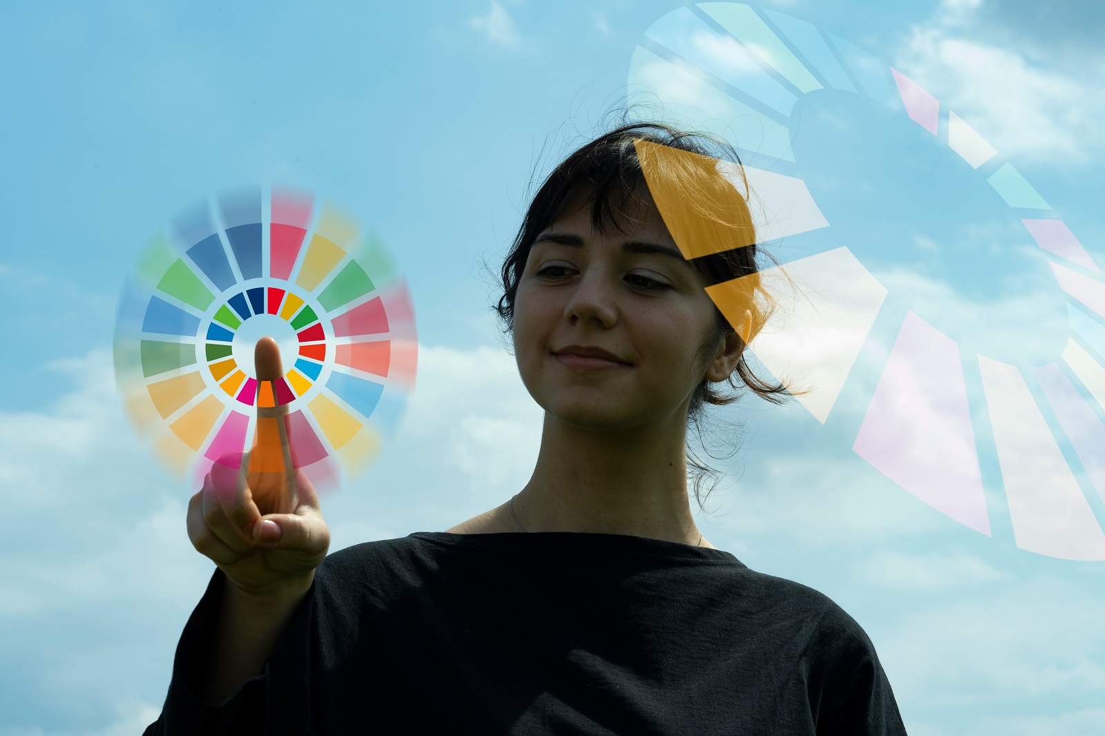 Eine Frau vor einem blauen Himmel tippt mit dem Finger in die Mitte des SDG-Kreises.